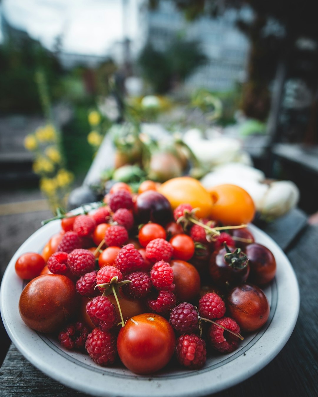Freshly harvested raspberries and tomatoes piled on a wooden table.